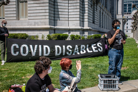 Covid Disables banner next to speaker in black t-shirt